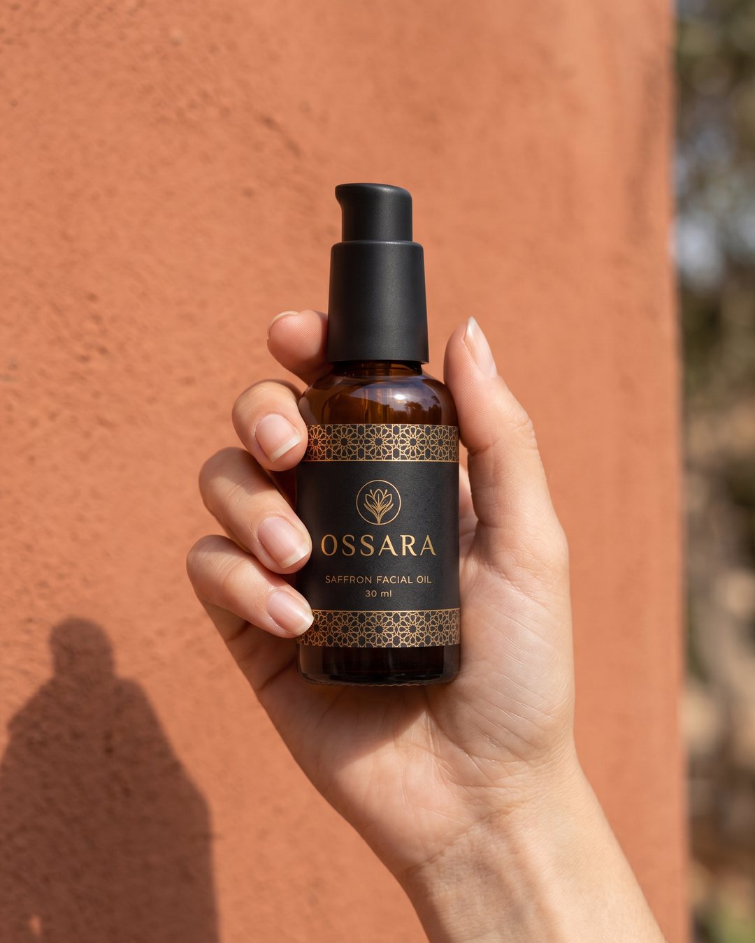 Hand holding the OSSARA bottle against a terracotta wall, social ad frame